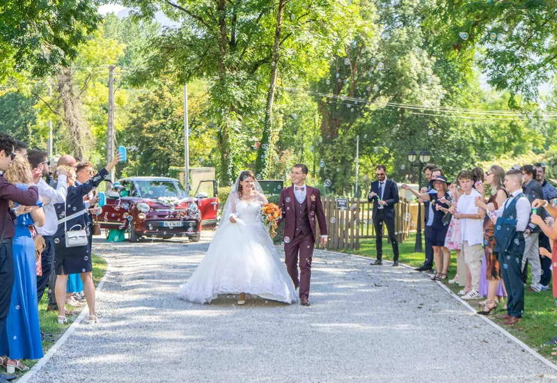 Les mariés remontent une allée de graviers entre leurs invités qui applaudissent.