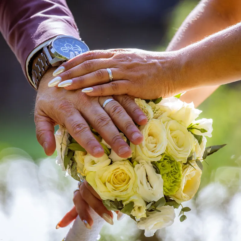 Les mains des mariés et leurs alliances posées sur le bouquet.