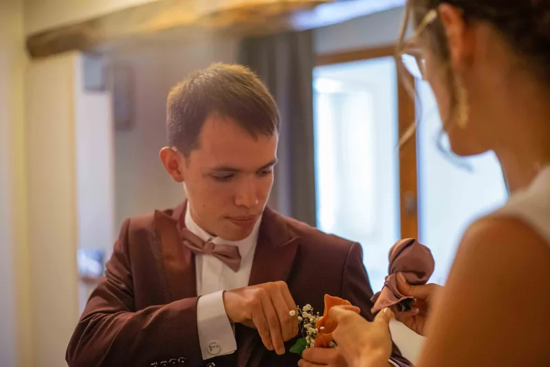 Préparatifs : on ajuste la boutonnière du marié en costume bordeaux.