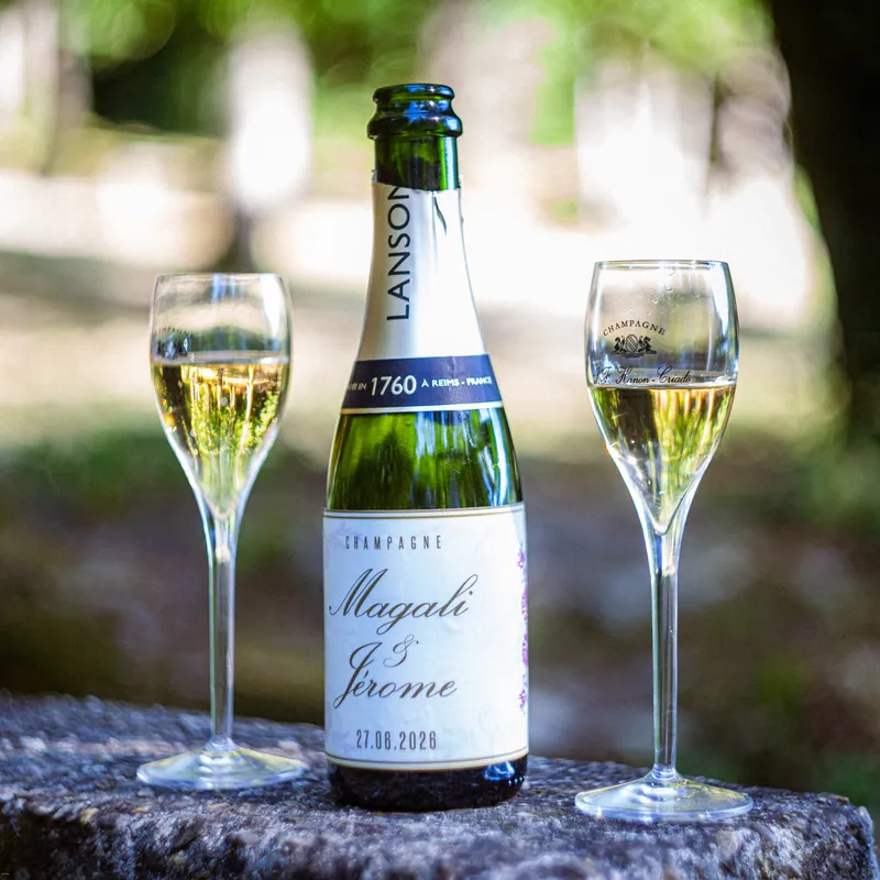 Bouteille de champagne personnalisée « Magali & Jérôme » entre deux flûtes.