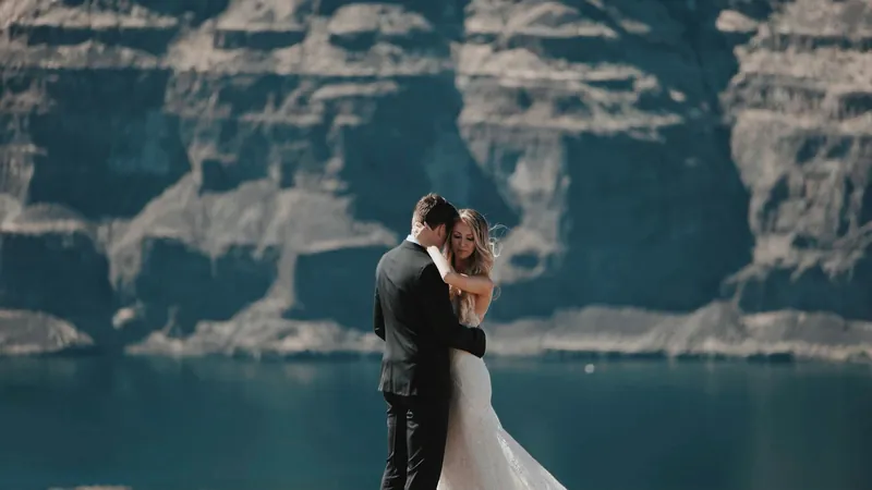 Couple enlacé au bord d’un lac, au pied de falaises.