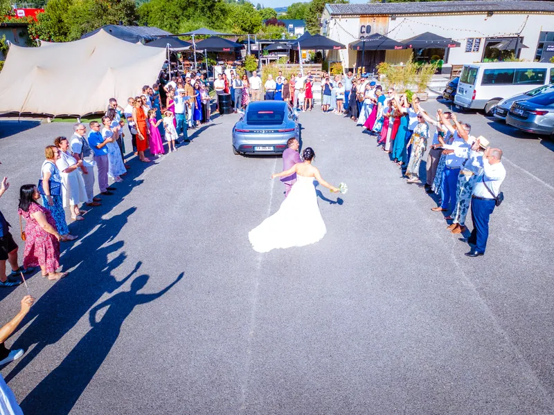 Vue de drone : la mariée remonte l’allée formée par les invités.