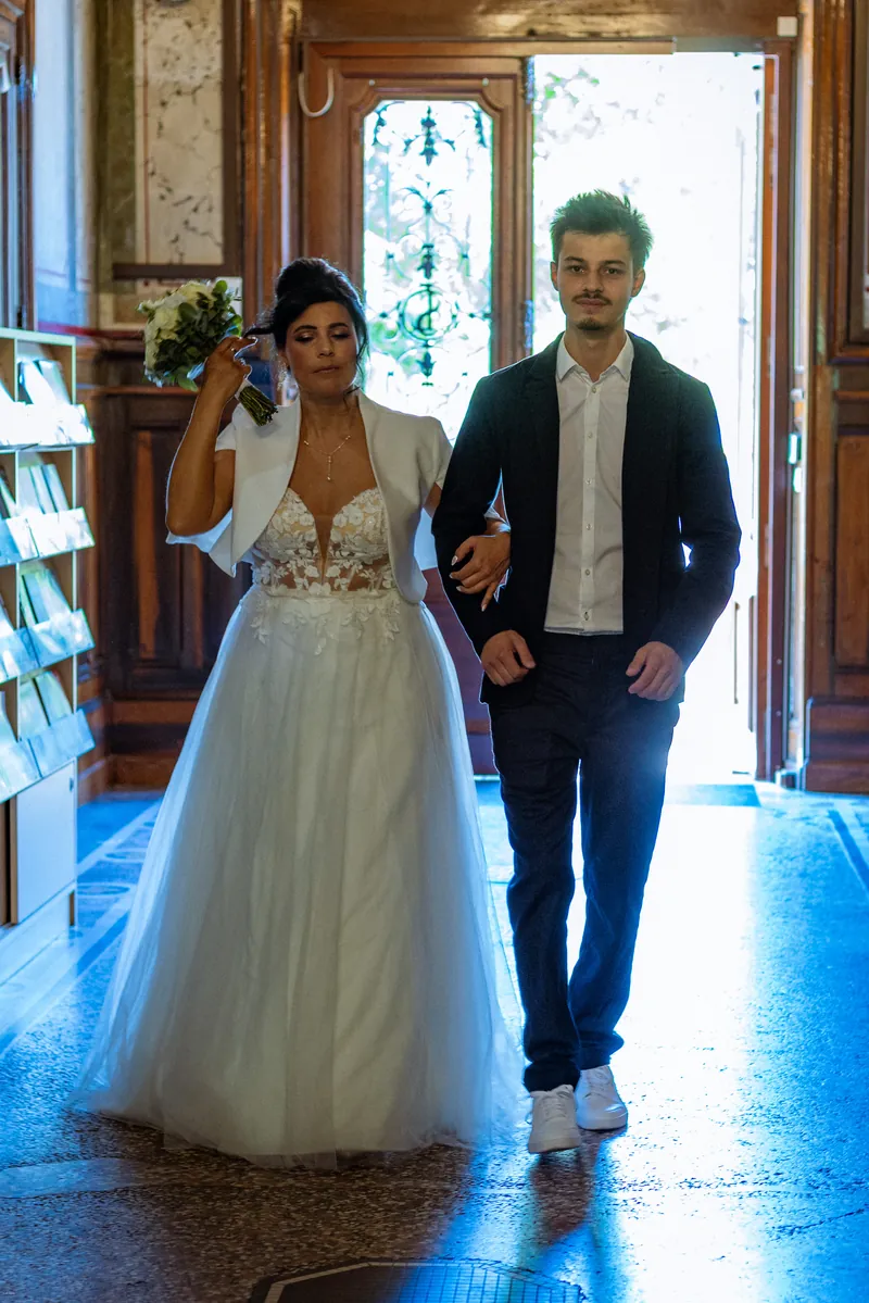 La mariée entre dans la mairie au bras d’un proche, à contre-jour.