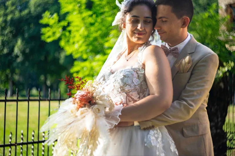 Le marié enlace la mariée par derrière, bouquet de fleurs séchées à la main.