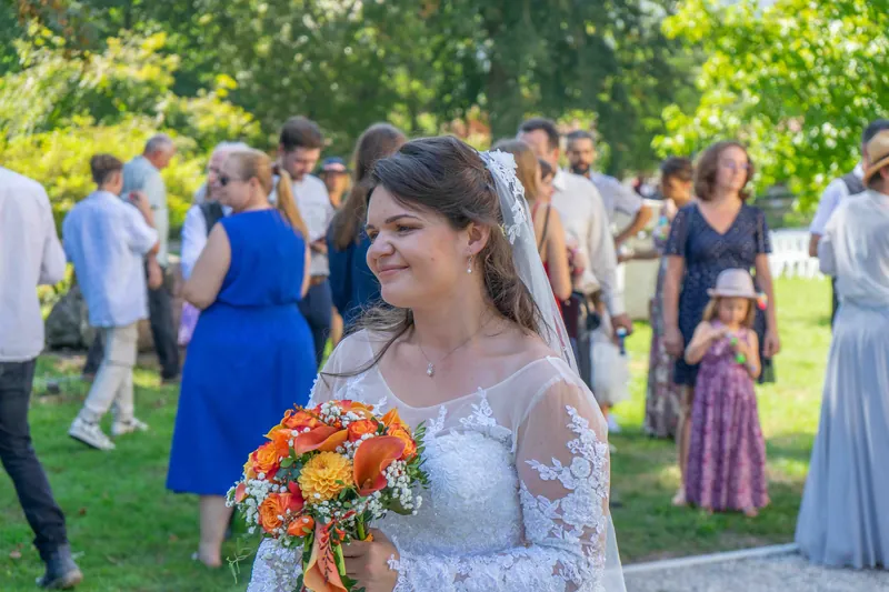 La mariée, bouquet orangé à la main, au milieu des invités.