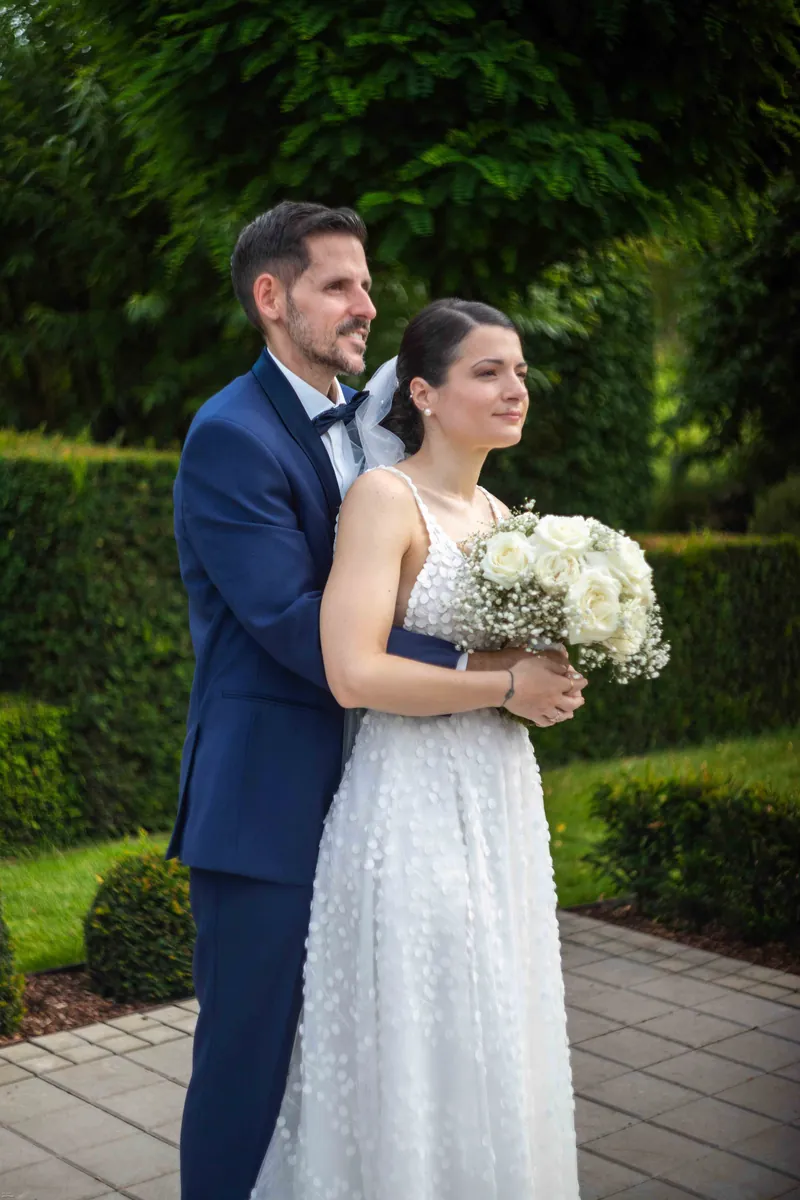 Portrait des mariés dans un jardin, la mariée tient un bouquet blanc.