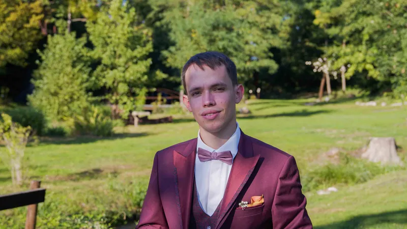 Portrait du marié en costume bordeaux dans un parc.