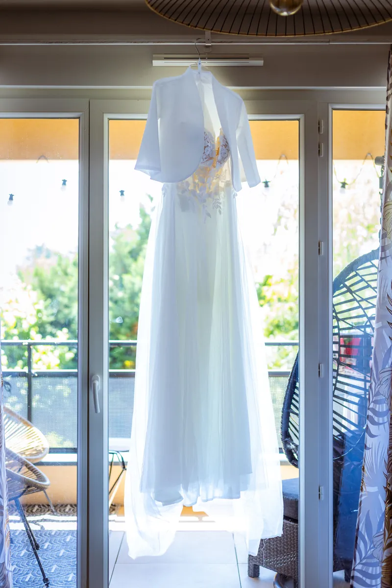 Préparatifs : la robe de mariée suspendue devant une baie vitrée.