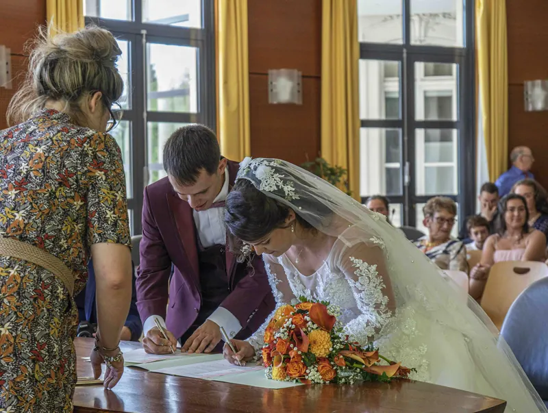 La mariée signe le registre à la mairie, le marié à ses côtés.