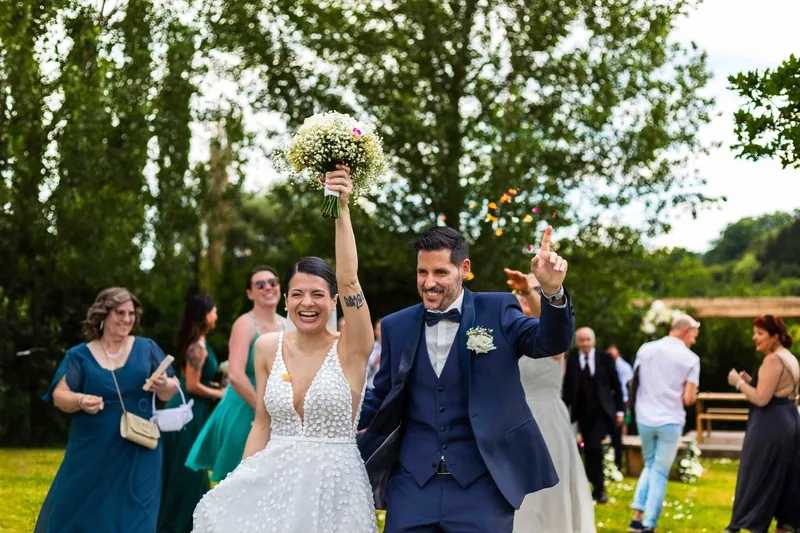 Sortie de cérémonie : la mariée brandit son bouquet au milieu des invités.